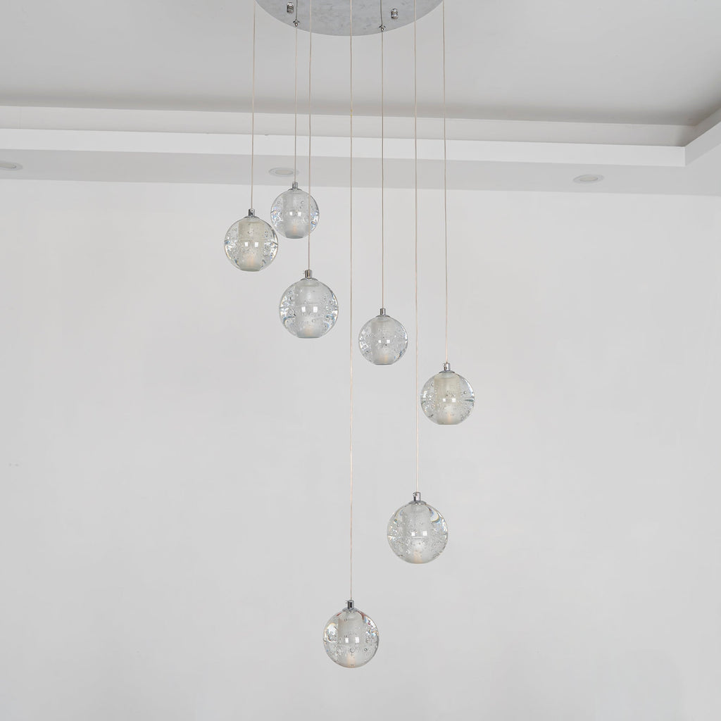 Unlit, the spheres of this Clérachic pendant light hang from a round chrome plate against a pale wall, clear and lightly bubbled.