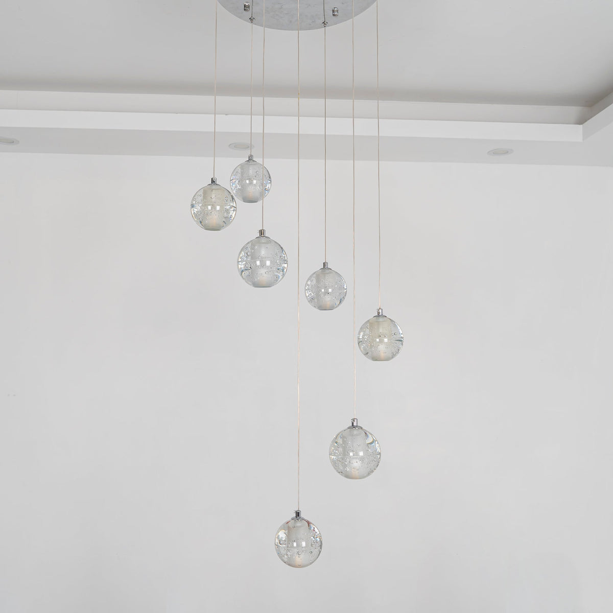 Unlit, the spheres of this Clérachic pendant light hang from a round chrome plate against a pale wall, clear and lightly bubbled.