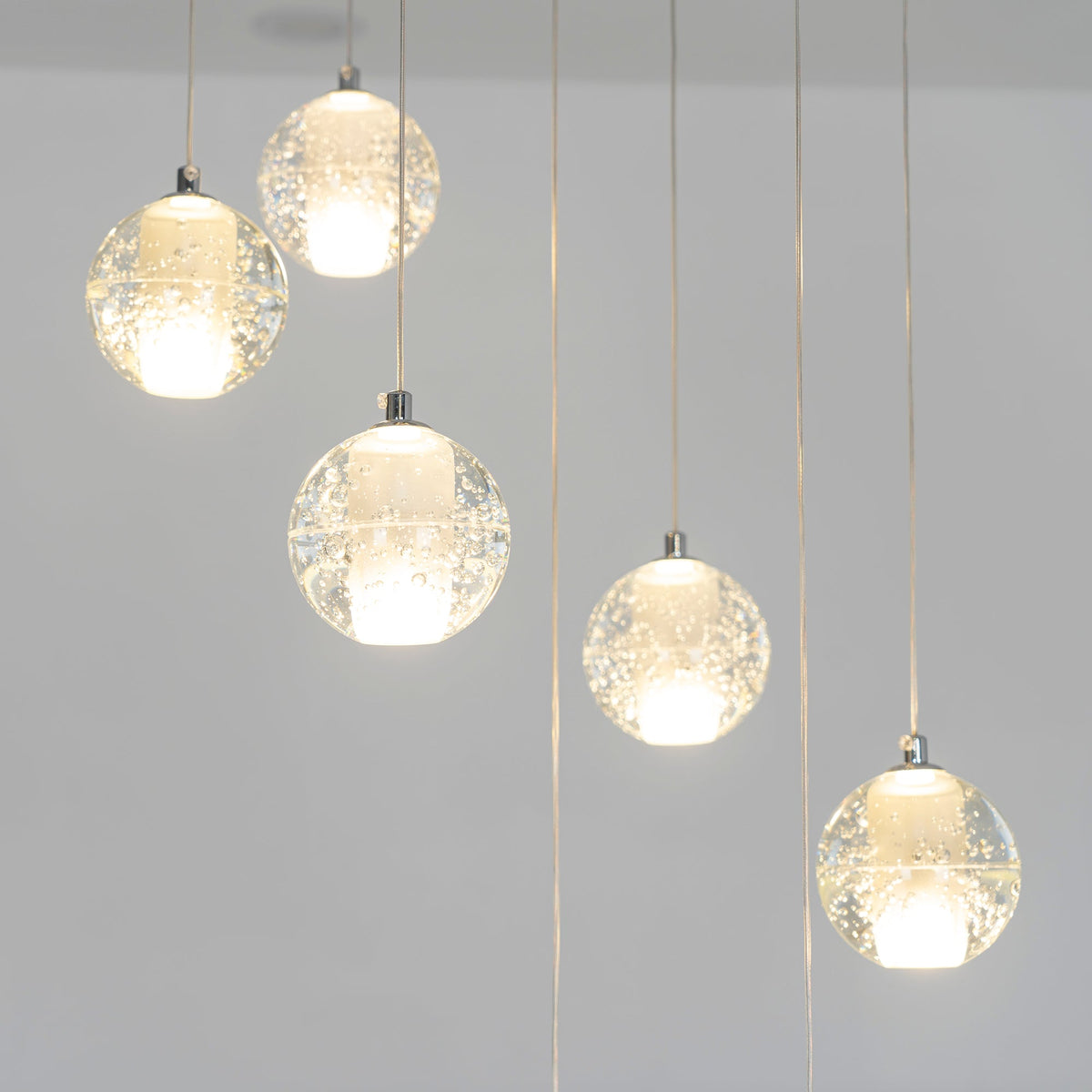 Lit spheres of this Clérachic pendant light hang at staggered heights, each with a warm white core, against a grey wall.