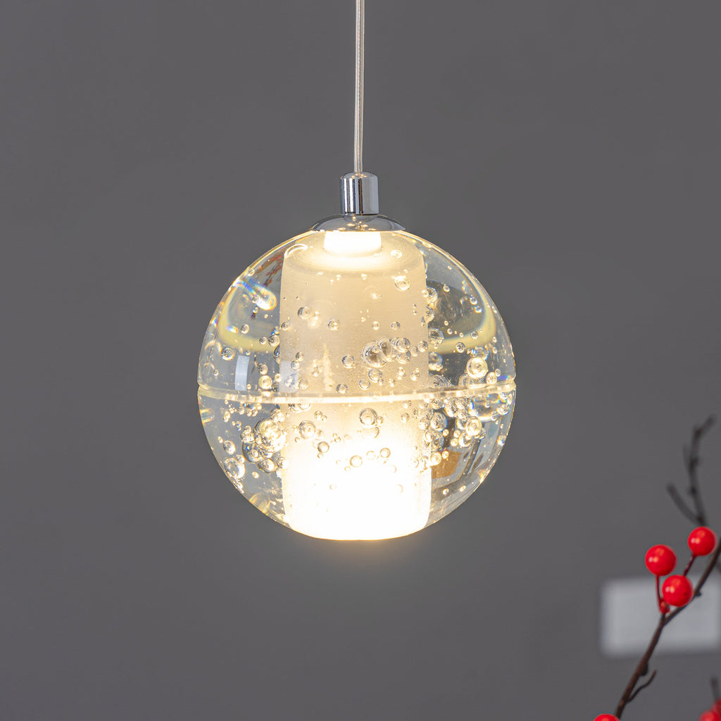 A single lit sphere of this Clérachic pendant light, clear bubbled glass around a frosted core, with a sprig of red berries at the edge.