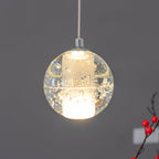A single lit sphere of this Clérachic pendant light, clear bubbled glass around a frosted core, with a sprig of red berries at the edge.