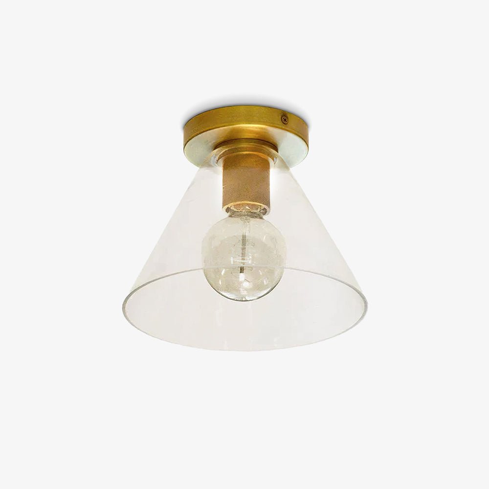 Brass flush ceiling light with a knurled socket, a bare round bulb and a clear conical glass shade, on a white backdrop, from Clérachic.