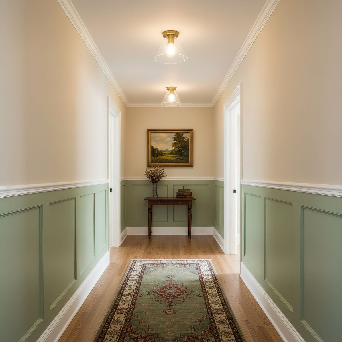Two brass ceiling lights with clear glass shades glow down a hallway with sage-green panelling and a patterned runner, from Clérachic.