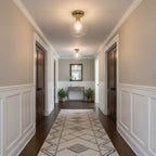 Glass-globe ceiling lights hang flush above a long panelled hallway with a geometric runner and a mirror at the end, from Clérachic.