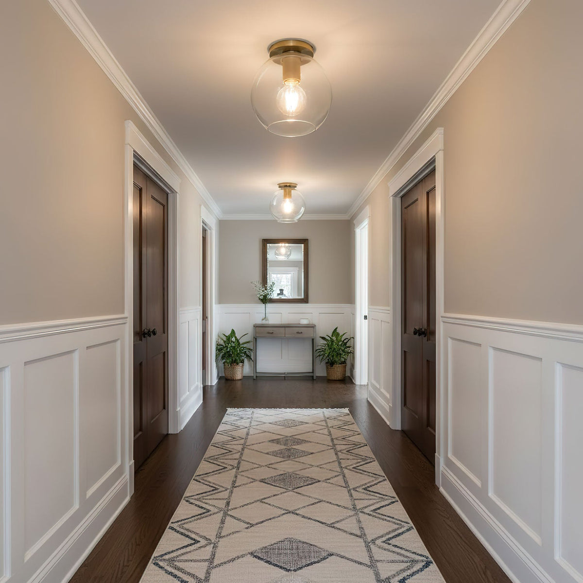 Glass-globe ceiling lights hang flush above a long panelled hallway with a geometric runner and a mirror at the end, from Clérachic.