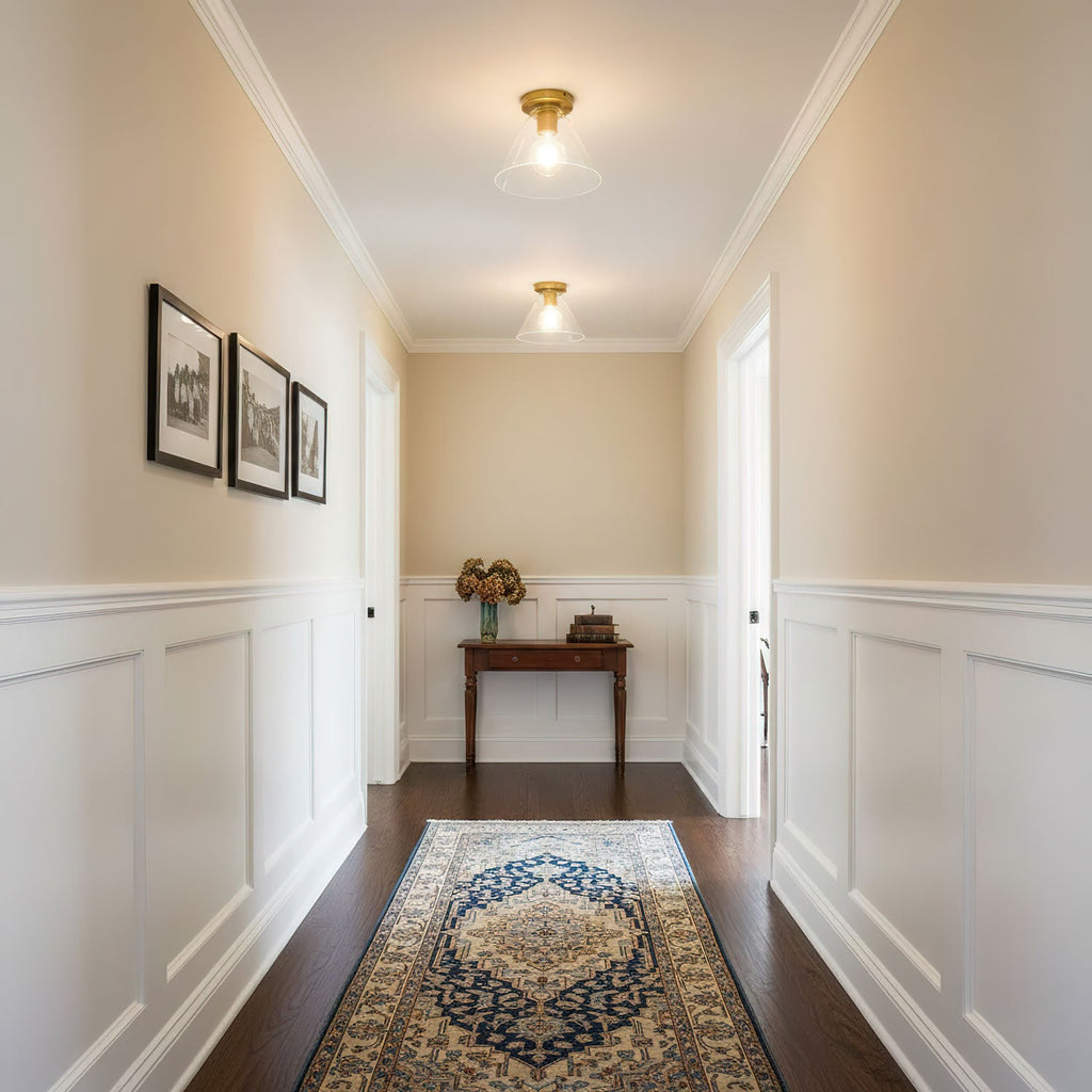 Looking down a cream hallway with white panelling and a blue patterned rug, a Clérachic flush mount glows on the ceiling.