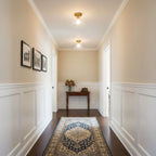 Looking down a cream hallway with white panelling and a blue patterned rug, a Clérachic flush mount glows on the ceiling.
