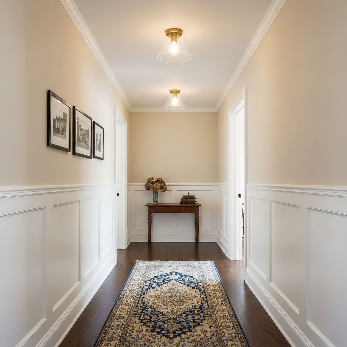Looking down a cream hallway with white panelling and a blue patterned rug, a Clérachic flush mount glows on the ceiling.