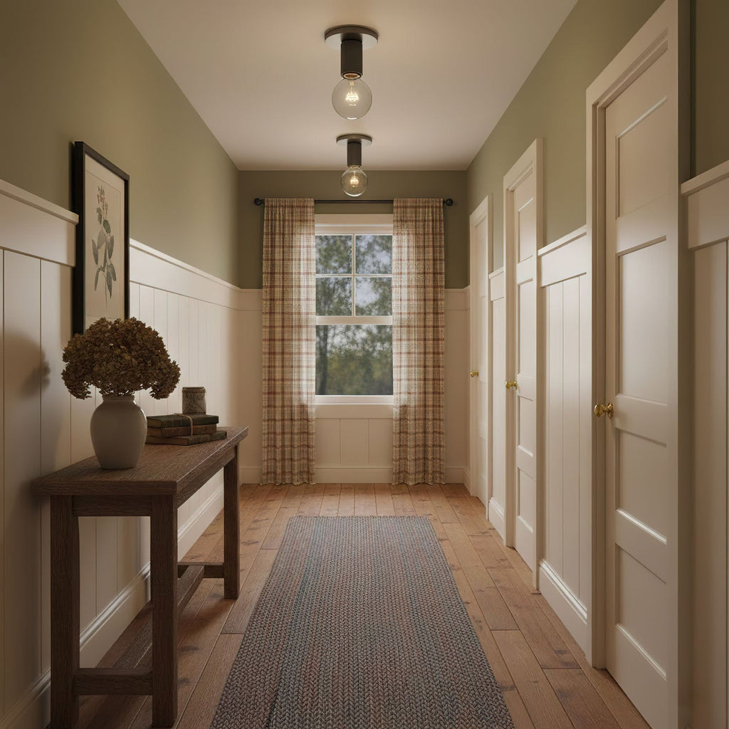 Two small flush lights with black fittings glow on a sage-green hallway ceiling above a console table with dried flowers, from Clérachic.