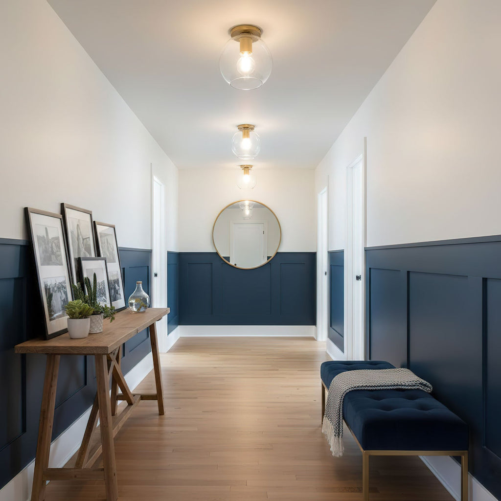 Three ceiling lights run along a navy-panelled hallway with a round mirror and a blue bench, a Clérachic flush mount.