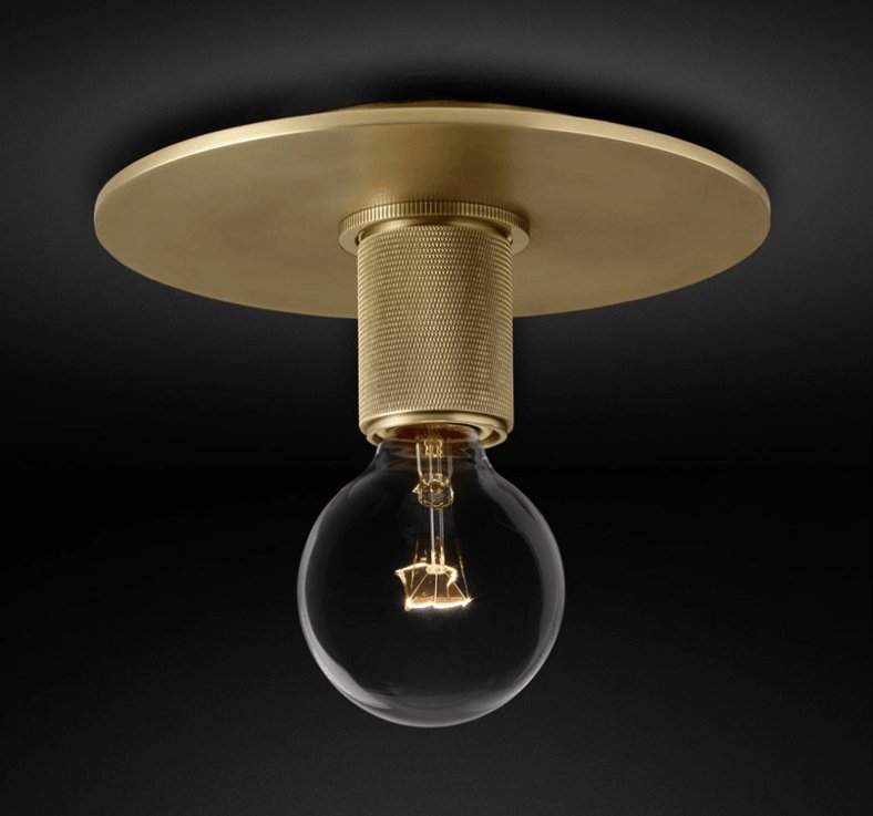 Wide brass ceiling plate with a knurled socket and a bare globe bulb lit warm, shown against black, a Clérachic flush mount.