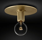 Wide brass ceiling plate with a knurled socket and a bare globe bulb lit warm, shown against black, a Clérachic flush mount.