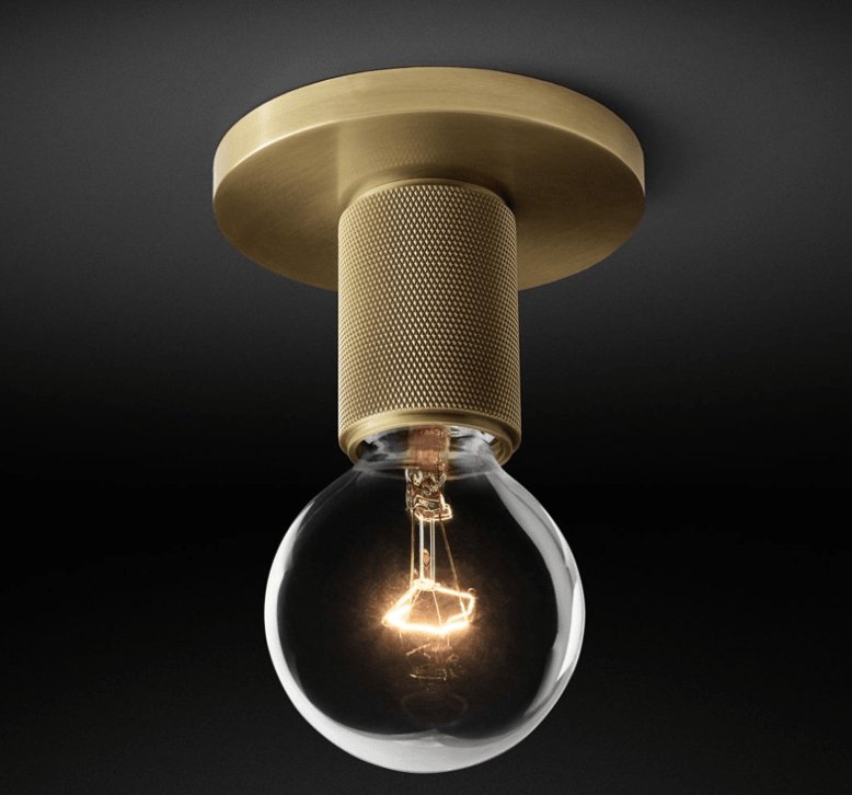 Close view of the knurled brass socket and a glowing filament bulb below the round brass plate, on this Clérachic flush mount.
