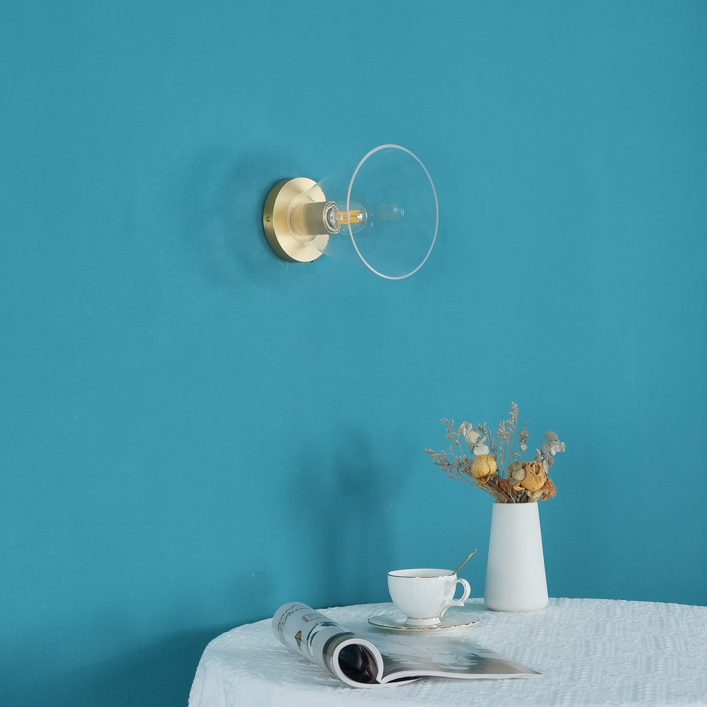 The same light unlit on a teal wall, its clear glass flare and brass plate visible above a small table, a Clérachic flush mount.