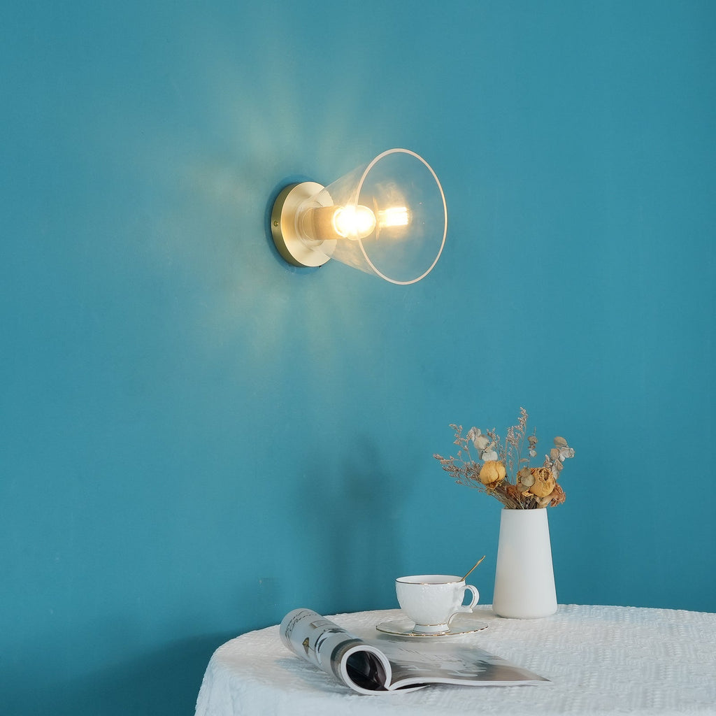 Lit bulb inside a clear flared glass shade on a bright teal wall, with a magazine and teacup on a table, from Clérachic.