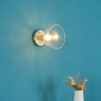 Closer view of a lit light with a brass plate and clear glass flare on a teal wall, with dried flowers below, a Clérachic flush mount.