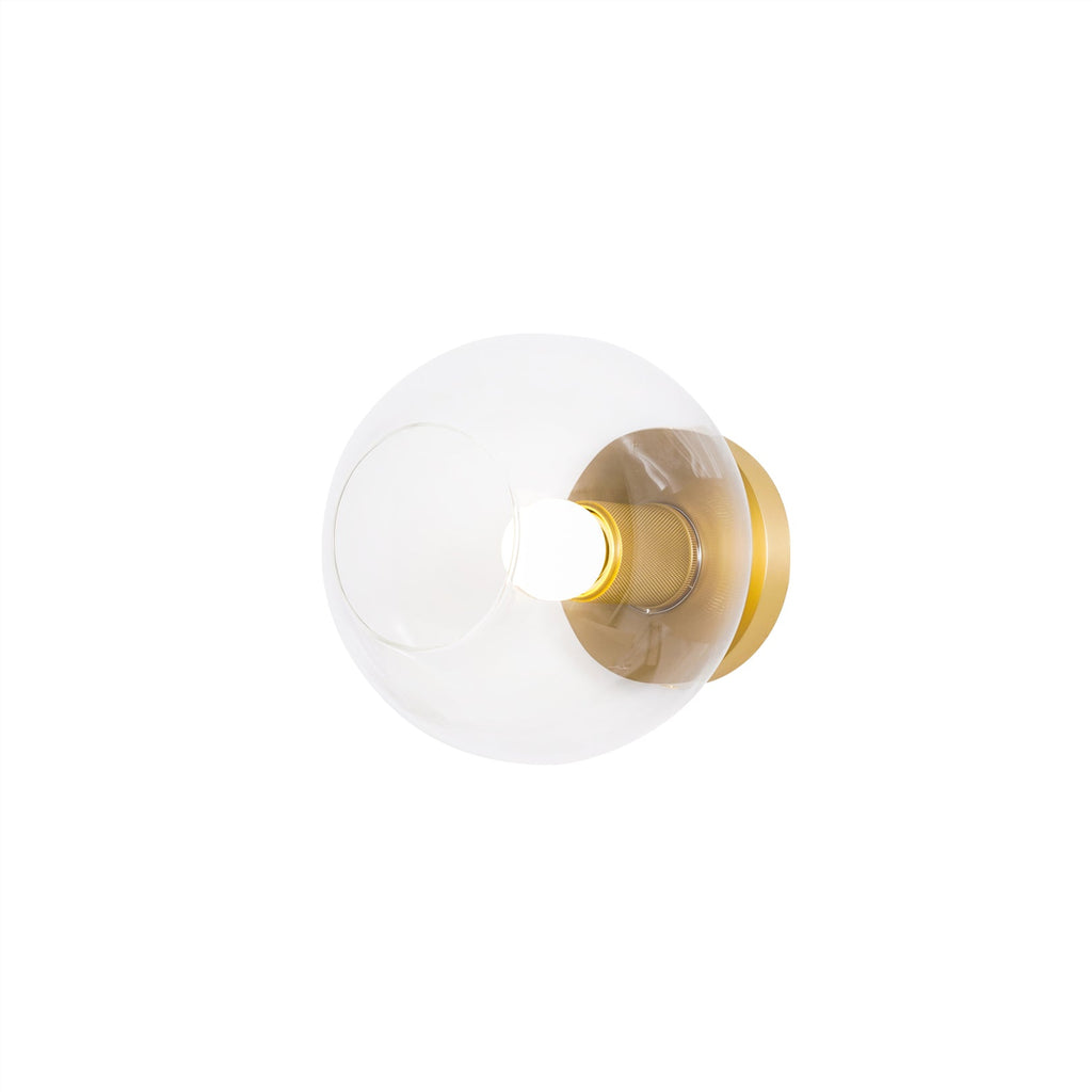 Round clear glass shade with a brass plate and a lit bulb, on a plain white background, a Clérachic flush mount.