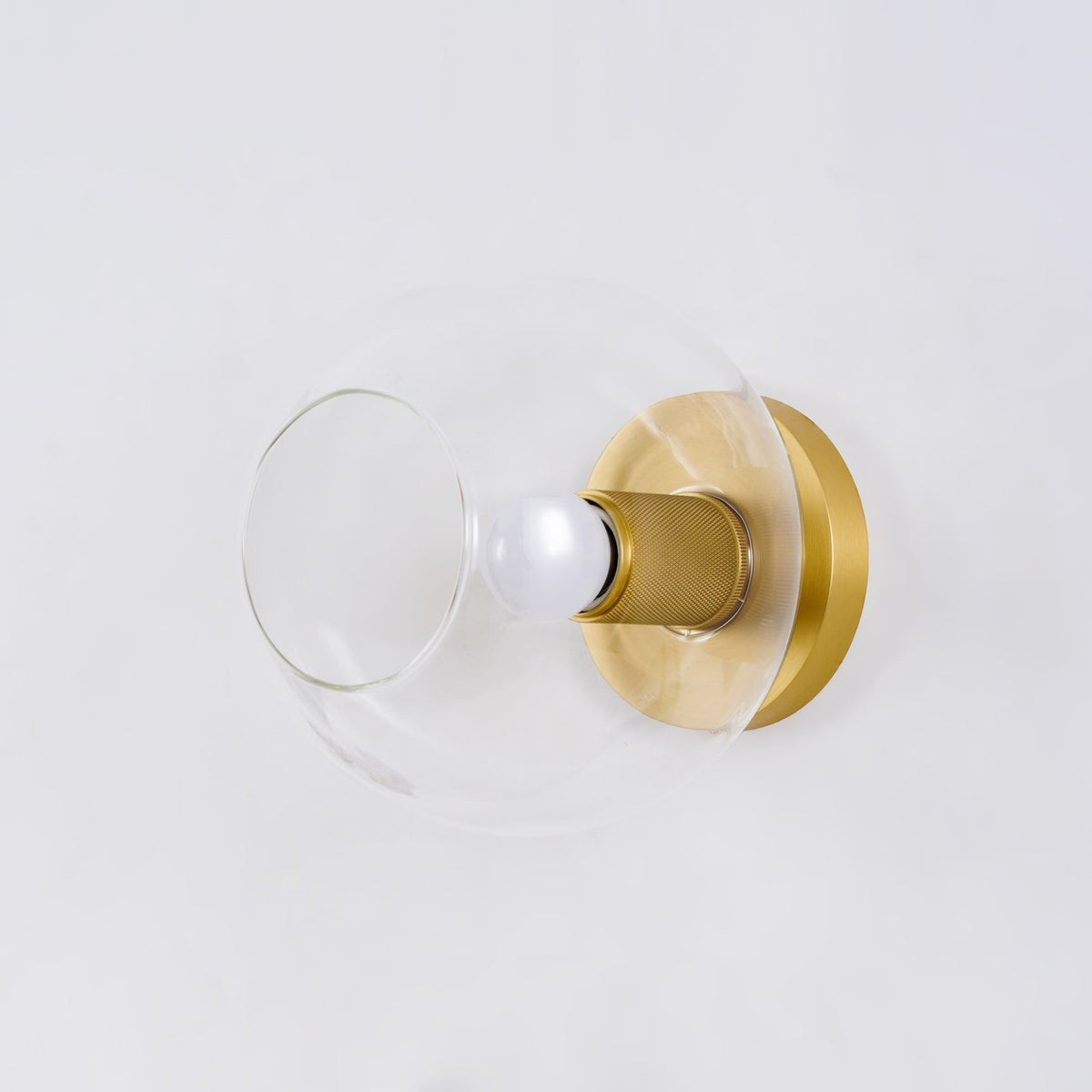 Close view of the clear glass globe with a brass backplate and a knurled brass socket holding a lit bulb, from Clérachic.