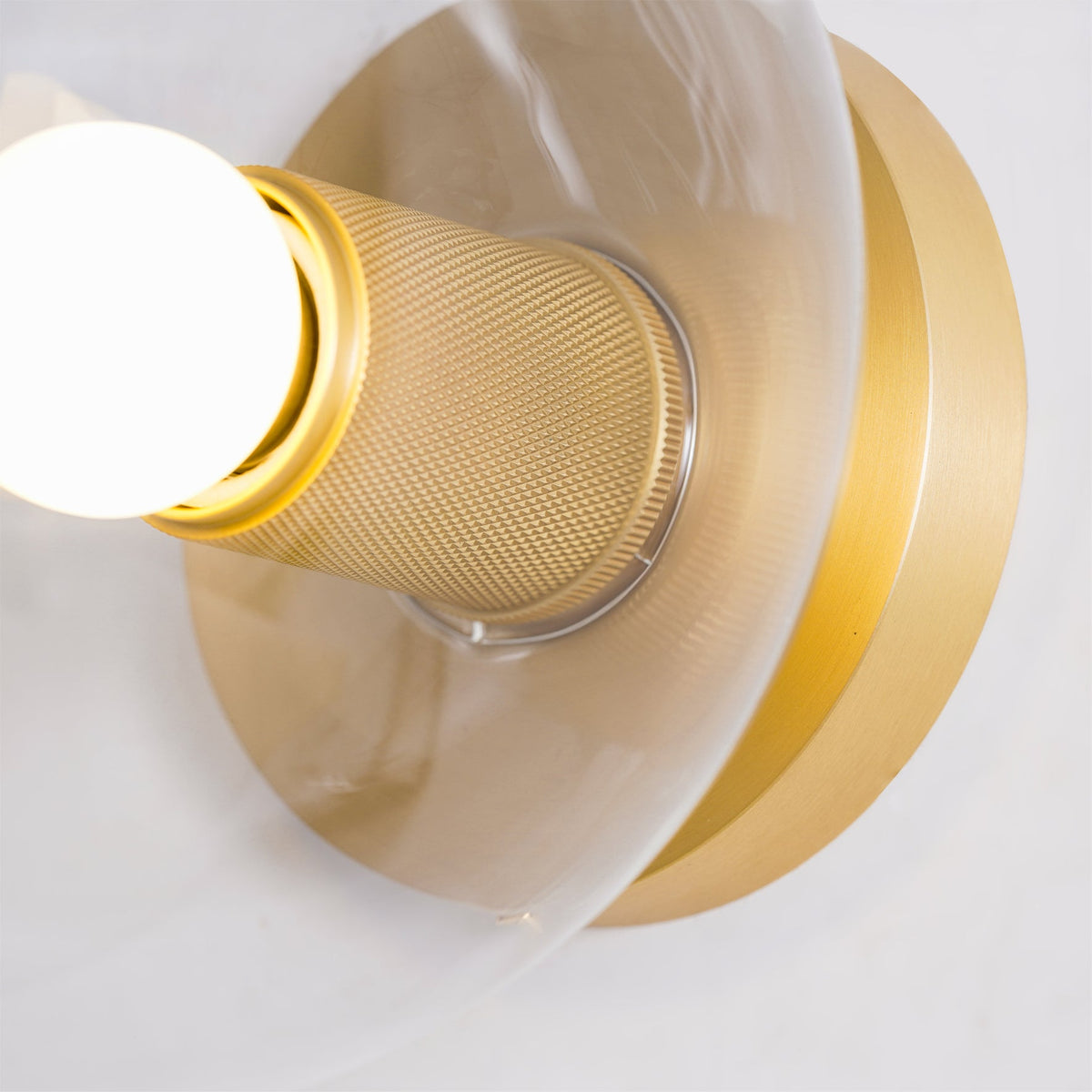 Very close view of the knurled brass socket and round backplate, with a glowing bulb at the left edge, on this Clérachic fitting.
