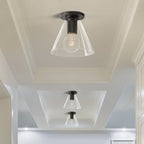 Black-fitted flush lights with clear glass shades on a panelled ceiling above a light hallway, a Clérachic flush mount.
