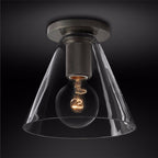 Black metal plate and knurled socket holding a filament bulb inside a clear conical glass shade, on a dark background, from Clérachic.