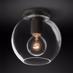 Clear glass globe around a glowing bulb, with a black plate and knurled black socket, against a dark backdrop, a Clérachic flush mount.