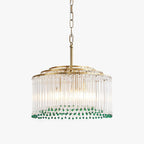A Clérachic clear glass rod chandelier with a gold tiered frame, green beads along the lower rim and a chain, on a white backdrop.