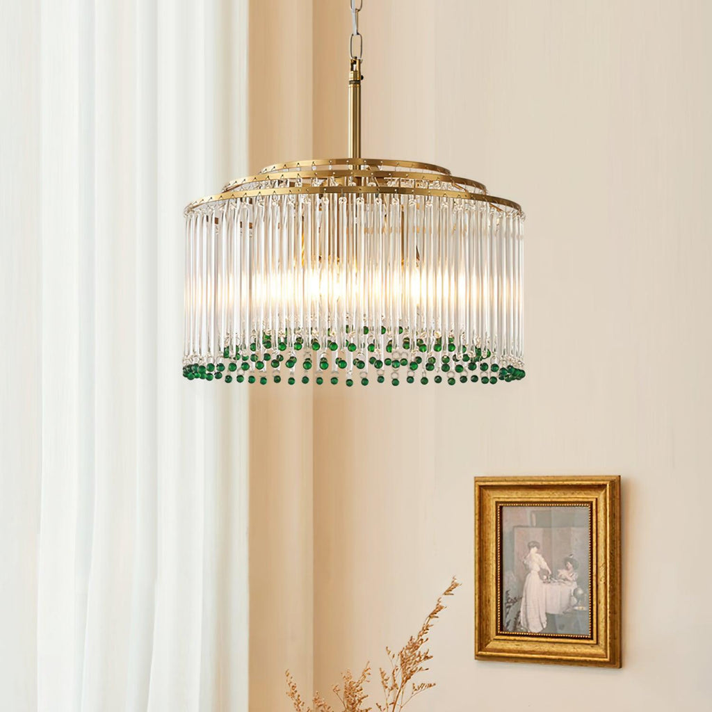 This Clérachic gold and glass chandelier hangs beside sheer curtains, with a gilt-framed painting on the wall behind it.