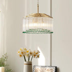 A Clérachic chandelier of clear glass rods and green beads hangs over a vase of daffodils and a chequered picture frame.