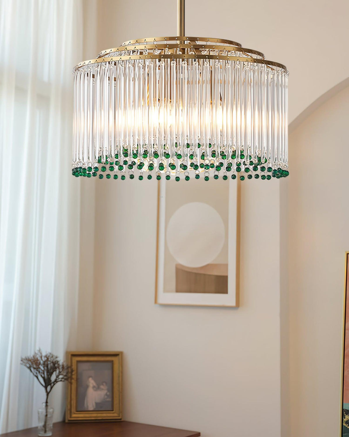 A Clérachic gold-framed glass rod chandelier in a bright room with a round framed print and sheer curtains.