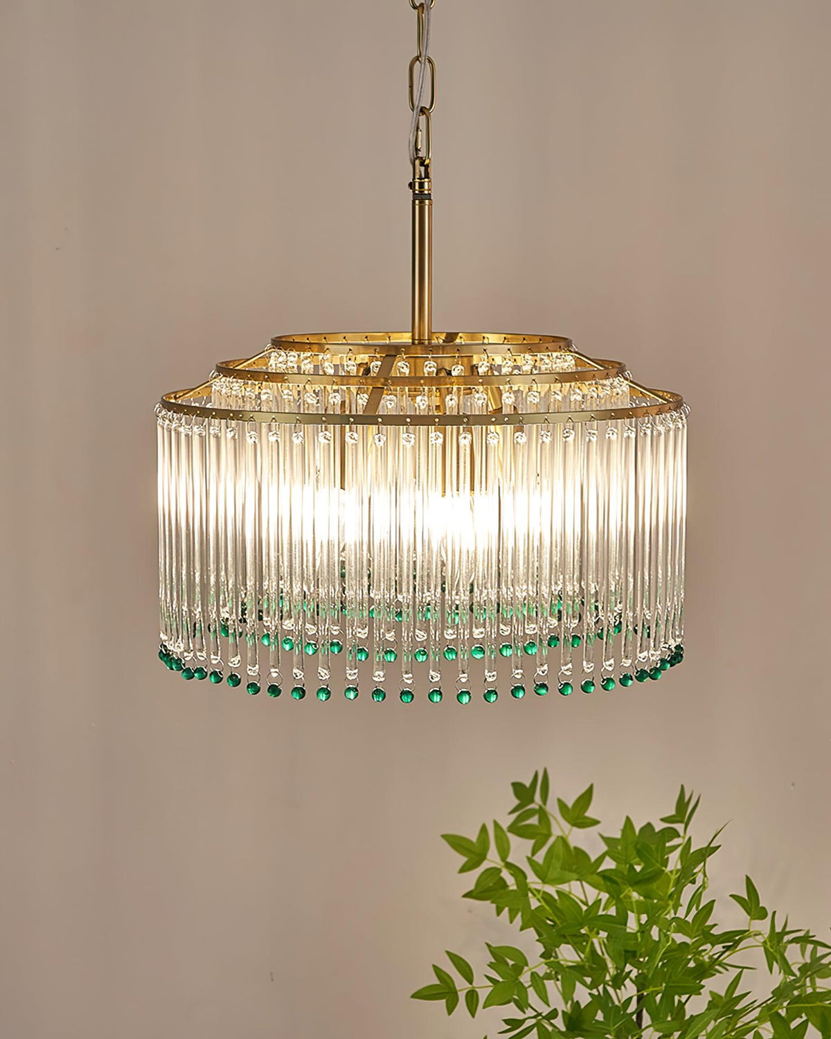 This Clérachic chandelier glows warmly against a taupe wall, its glass rods catching the light above a few green leaves.