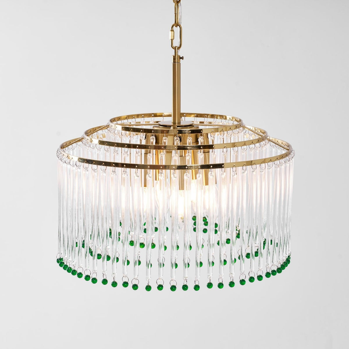 Angled close view of this Clérachic chandelier, with three tiers of gold rings above clear glass rods and green beads.