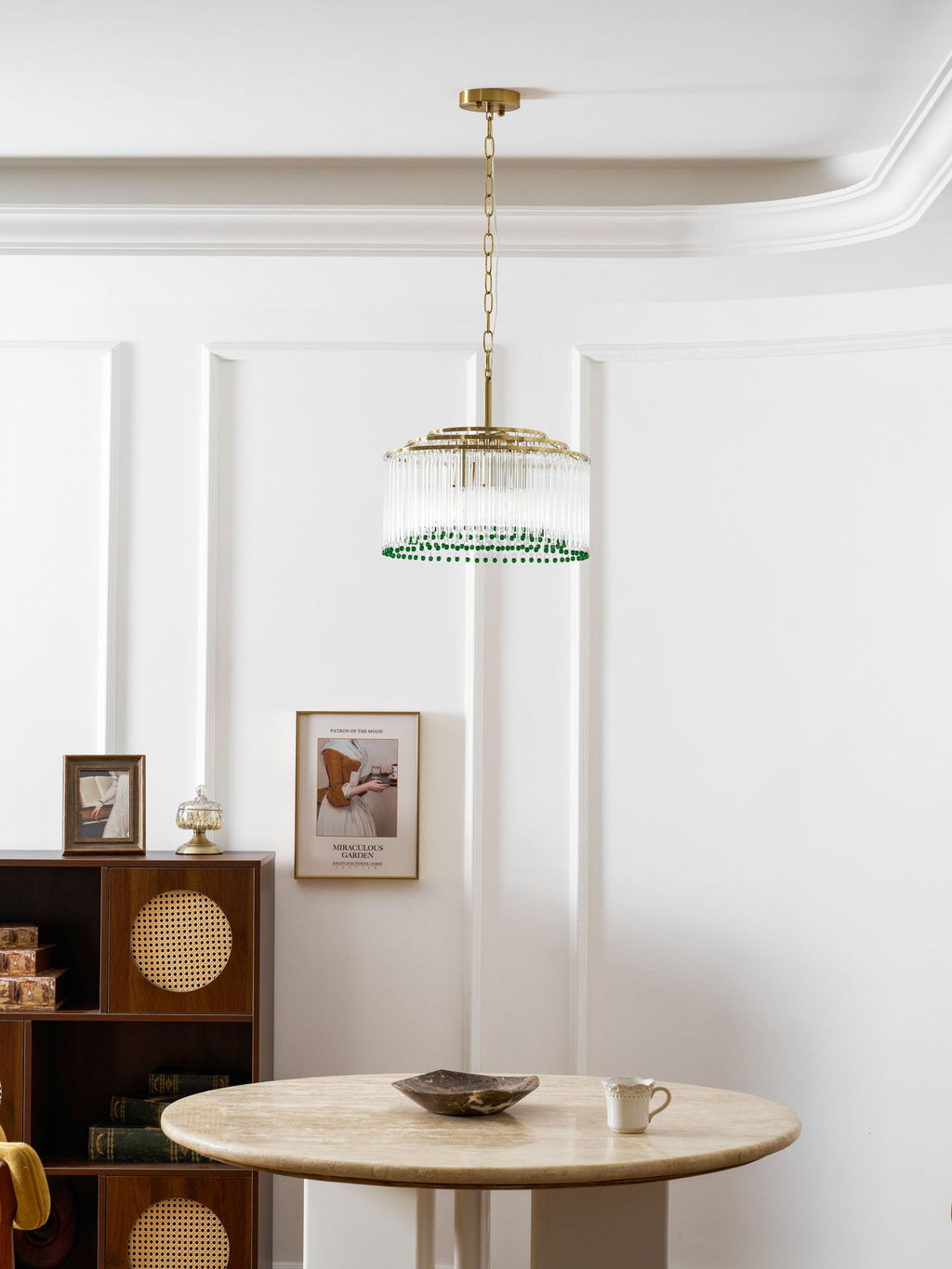 A small Clérachic glass rod chandelier hangs from a gold ceiling plate in a white panelled dining room above a round marble table.