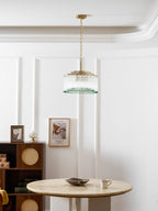 A small Clérachic glass rod chandelier hangs from a gold ceiling plate in a white panelled dining room above a round marble table.