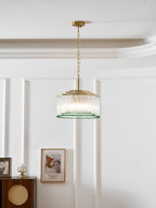 In a panelled white room, this Clérachic gold and glass chandelier hangs above a rattan-front cabinet and a framed print.