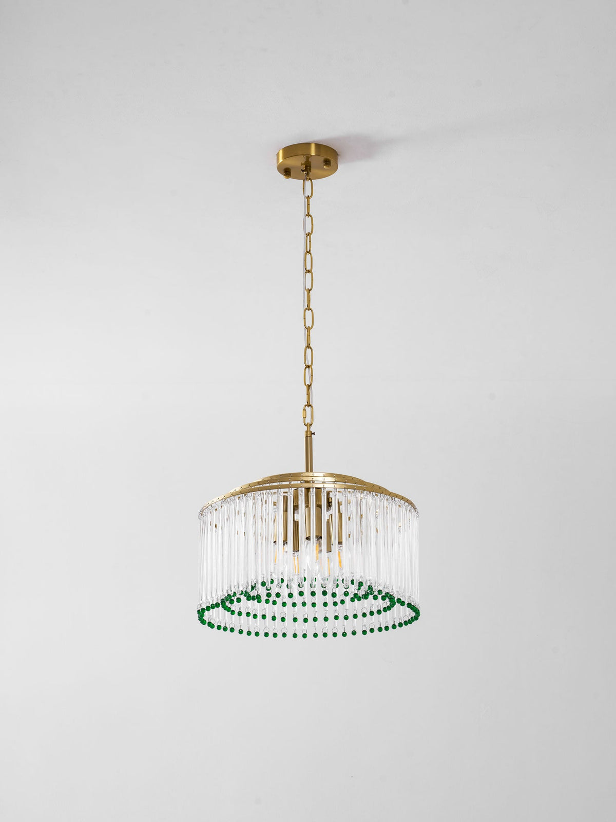 This Clérachic chandelier hangs on a gold chain from a round ceiling plate, shown against a plain grey wall.