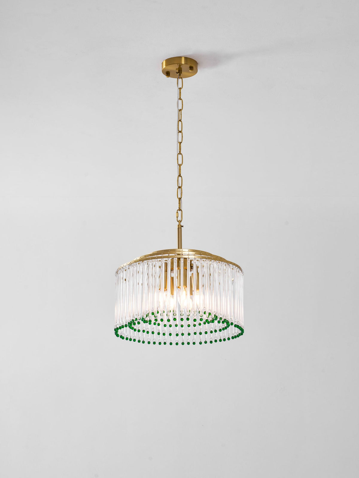 A Clérachic chandelier with candle-style bulbs inside a drum of glass rods, ringed with green beads, on a grey background.