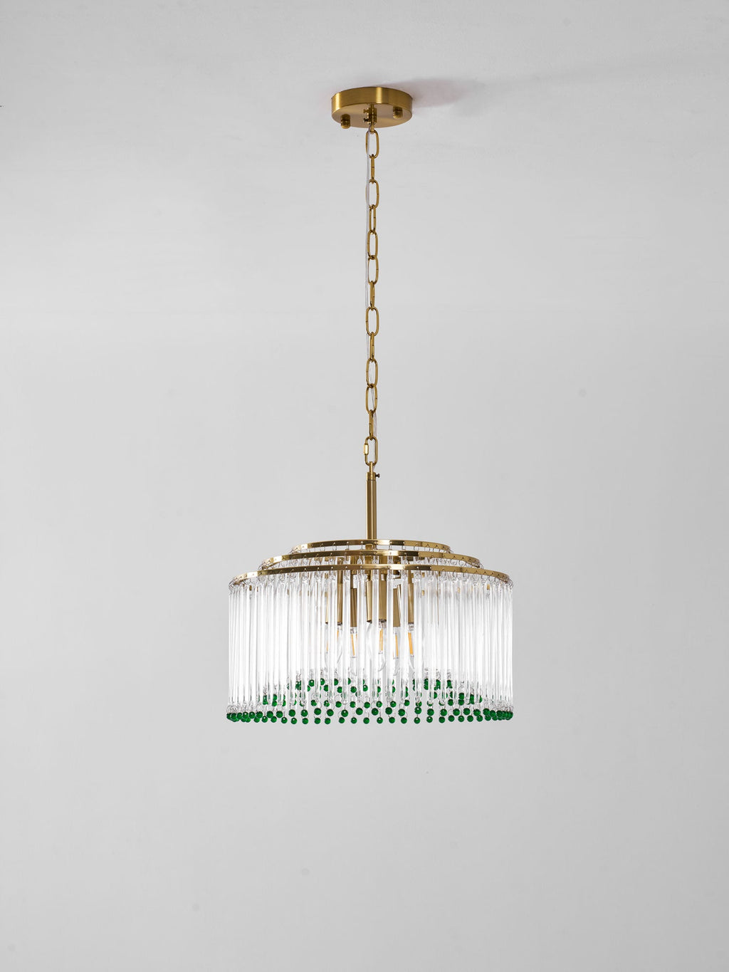 Side view of this Clérachic chandelier, with stepped gold rings above its clear glass rods, on a plain grey wall.