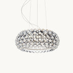 A wide, low pendant covered in clear acrylic spheres hangs from fine cables against a plain white backdrop, shown as this Clérachic pendant.