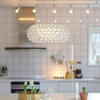 A clear sphere dome pendant hangs in a white-tiled kitchen with track spotlights, candles and a vase of hyacinths below, from Clérachic.