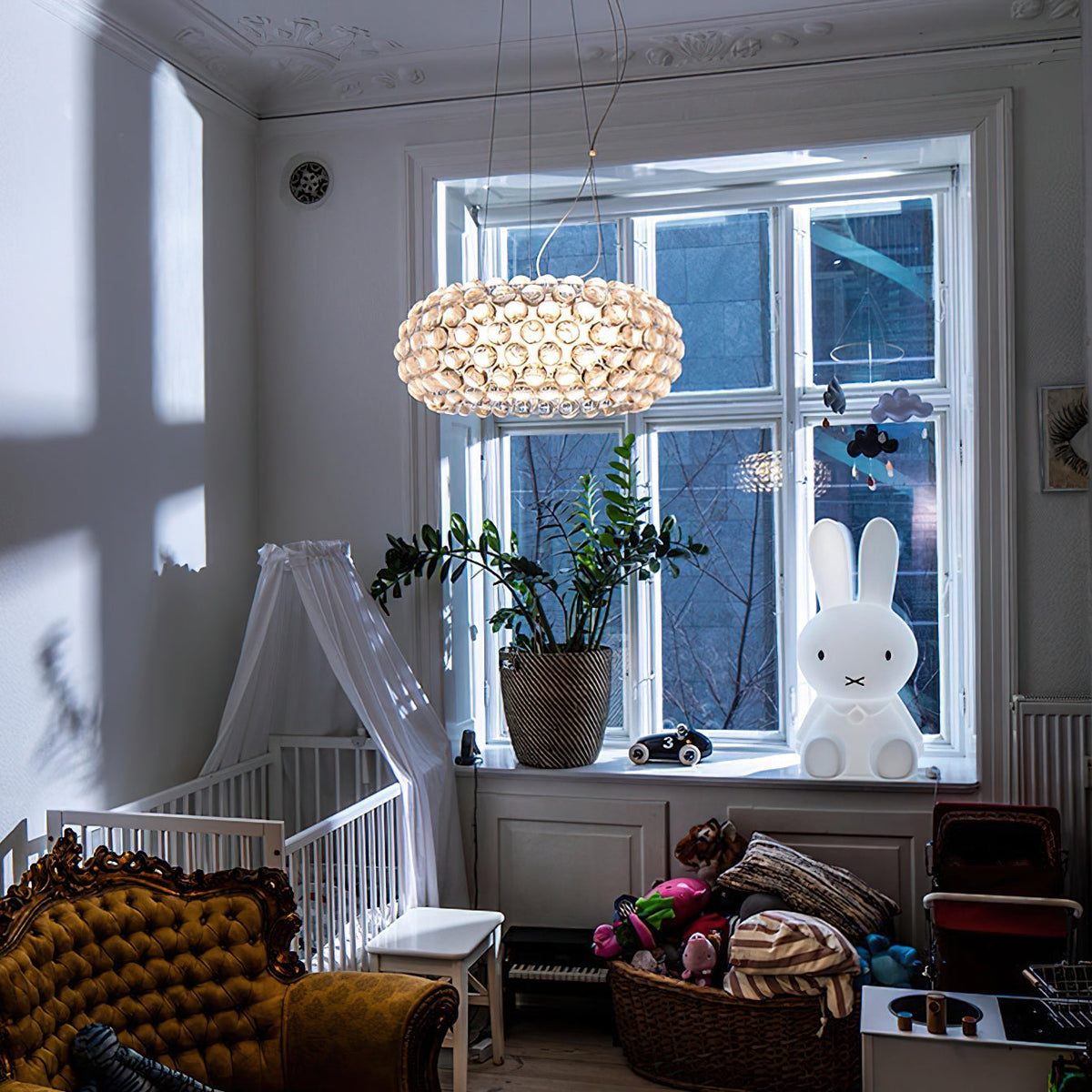 A clear sphere pendant hangs before a tall white-framed window in a child's room with a cot and a bunny lamp, from Clérachic.