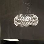 A clear sphere pendant glows against a dark grey plaster wall, its spheres reflecting the light, shown as this Clérachic pendant.