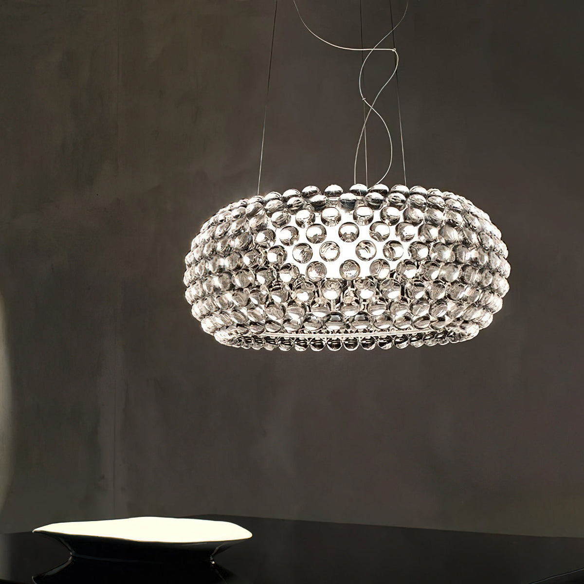 A clear sphere pendant glows against a dark grey plaster wall, its spheres reflecting the light, shown as this Clérachic pendant.