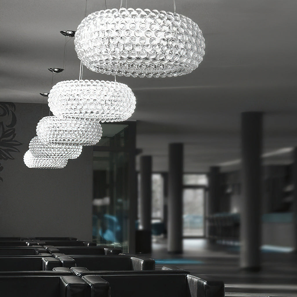 A line of clear sphere pendants of falling sizes hangs through a dark lounge with rows of black seating, from Clérachic.