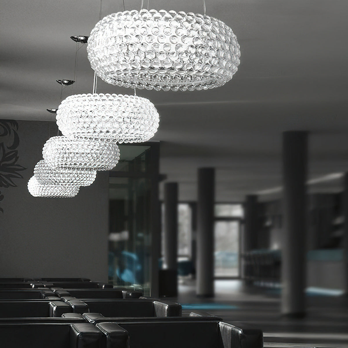 A line of clear sphere pendants of falling sizes hangs through a dark lounge with rows of black seating, from Clérachic.