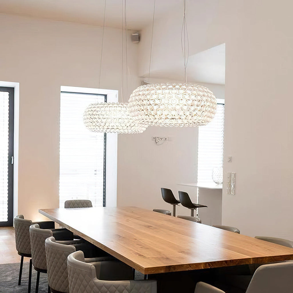 Two clear sphere pendants hang above a long oak table and quilted chairs in a white room with tall windows, from Clérachic.