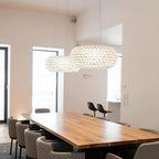 Two clear sphere pendants hang above a long oak table and quilted chairs in a white room with tall windows, from Clérachic.
