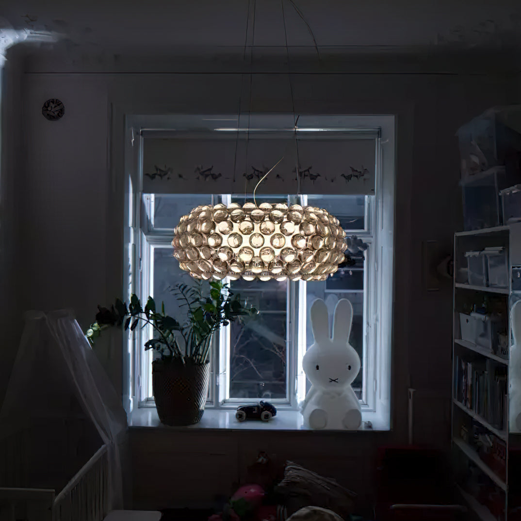 A sphere-covered pendant glows warm in a dim room, in front of a window with a plant and a bunny lamp, from Clérachic.