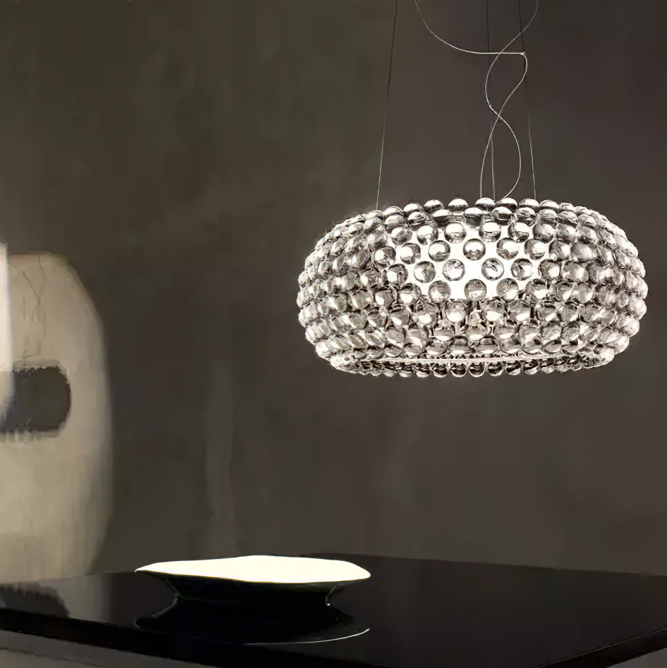 A clear sphere pendant glows against a dark grey wall above a black table with a white dish, from Clérachic.