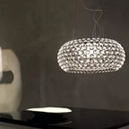 A clear sphere pendant glows against a dark grey wall above a black table with a white dish, from Clérachic.